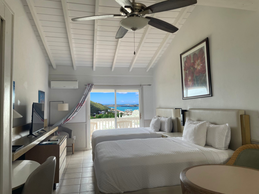 Twin room at Boundless Bliss Hotel, vaulted white ceiling and sliding door onto a balcony above Charlotte Amalie harbour